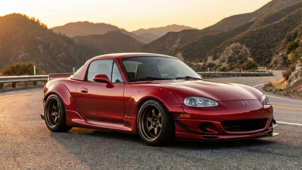 Mazda MX-5 NB rouge équipée d’un kit carrosserie large, posée sur une route de montagne au coucher du soleil