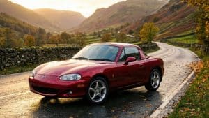 Mazda MX-5 NB rouge sur route de montagne au coucher du soleil