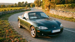 Mazda MX-5 NB verte d'occasion, avec panneau 'À VENDRE', sur une route de campagne en automne