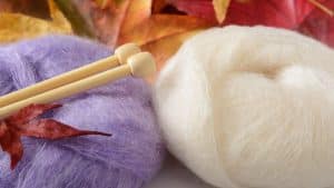 Pelotes de mohair violet et écru avec aiguilles à tricoter, ambiance automnale