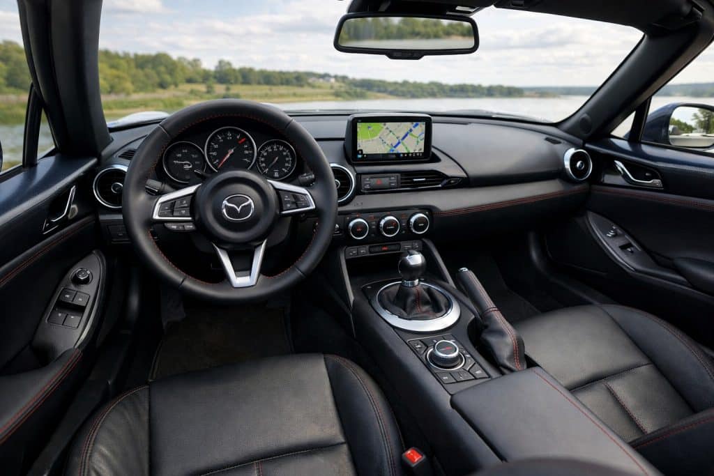 Intérieur d’une Mazda MX-5 décapotée, vue depuis le poste de conduite avec volant sport, écran central et sellerie en cuir noir.