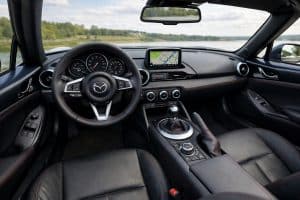 Intérieur d’une Mazda MX-5 décapotée, vue depuis le poste de conduite avec volant sport, écran central et sellerie en cuir noir.