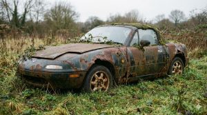 Mazda MX-5 ancienne abandonnée, fortement rouillée et envahie par la végétation dans un champ à l’abandon