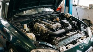 Moteur d’une Mazda MX-5 capot ouvert, photographié dans un atelier mécanique lors d’une intervention d’entretien.