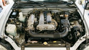 Moteur de Mazda MX-5 NBFL photographié de face, capot ouvert, montrant le bloc moteur DOHC 1.8L et ses composants dans un compartiment moteur d'une voiture grise