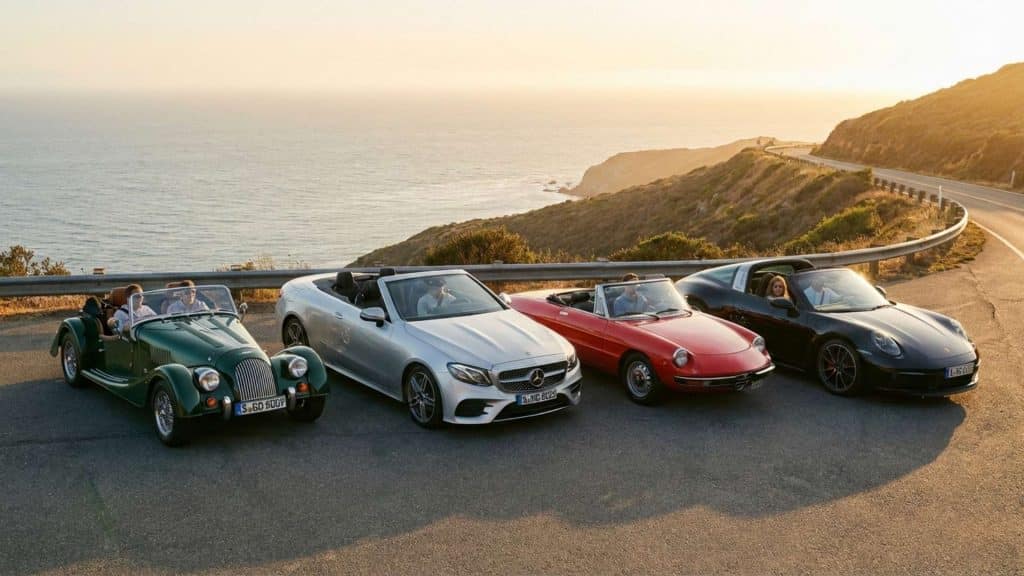 Alignement de quatre voitures de sport découvrables illustrant les différences de design entre les styles roadster, cabriolet, spider et targa en bord de mer