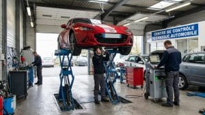 Mazda MX-5 rouge en cours de contrôle technique dans un centre automobile avec techniciens et équipements professionnels