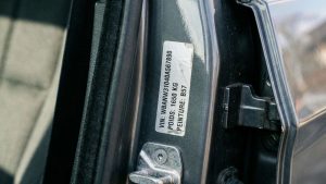 Étiquette VIN sur le montant de porte d’une voiture, avec numéro de châssis, poids et code peinture, près de la gâche de verrouillage.
