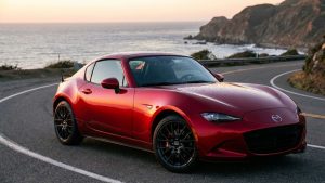Mazda MX-5 RF rouge stationnée sur une route côtière au coucher du soleil, avec l’océan et des falaises en arrière-plan.