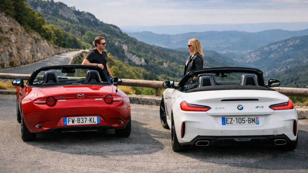 Mazda MX-5 rouge et BMW Z4 blanche arrêtées au belvédère avec deux conducteurs profitant d’un paysage montagneux
