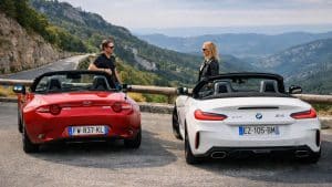 Mazda MX-5 rouge et BMW Z4 blanche arrêtées au belvédère avec deux conducteurs profitant d’un paysage montagneux