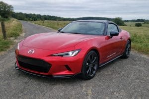 Photo amateur réaliste d’une Mazda MX-5 électrique NE 2027 sur une route de campagne, prise au smartphone par temps couvert