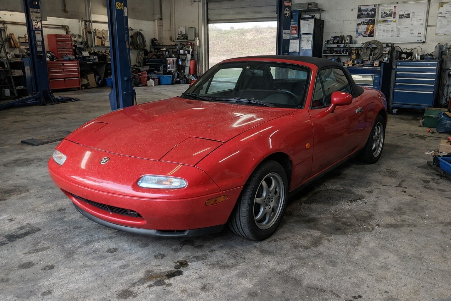 Mazda MX-5 NA rouge dans un garage mécanique professionnel, lumière naturelle, ambiance atelier