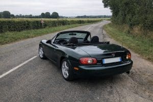 Photo réaliste d’une Mazda MX-5 NBFL verte capote ouverte sur une petite route de campagne française, lumière naturelle et rendu smartphone