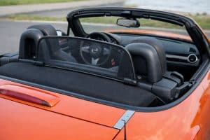 Windschott noir en mesh installé derrière les sièges d’une Mazda MX-5 NC orange, capote ouverte, vue arrière de l’habitacle