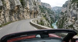 Vue depuis le siège passager d'une Mazda MX-5 ND rouge décapotée, regardant une route étroite et sinueuse taillée dans la falaise des Gorges du Verdon