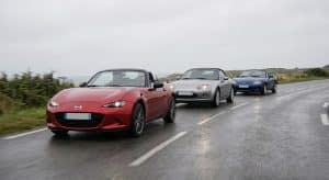 Un convoi de trois Mazda MX-5 (une ND rouge, une NC argentée et une NB bleue) roulant en ligne sur une route côtière mouillée en Bretagne lors d'une sortie club