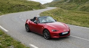Mazda MX-5 ND rouge décapotée roulant dans un col sinueux des Alpes françaises lors d'un roadtrip