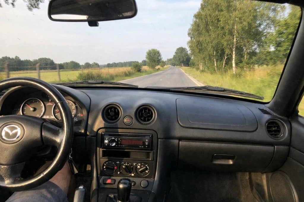 Vue intérieure d’une Mazda MX-5 NBFL en roulant sur une route de campagne en été, photo réaliste prise depuis le siège passager