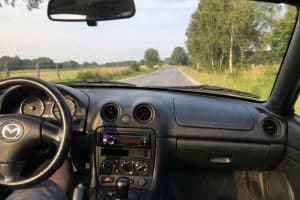 Vue intérieure d’une Mazda MX-5 NBFL en roulant sur une route de campagne en été, photo réaliste prise depuis le siège passager