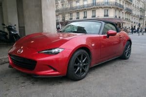 Photo d’une Mazda MX-5 ND rouge en location à Paris, stationnée en ville sous un ciel couvert, vue avant trois-quarts