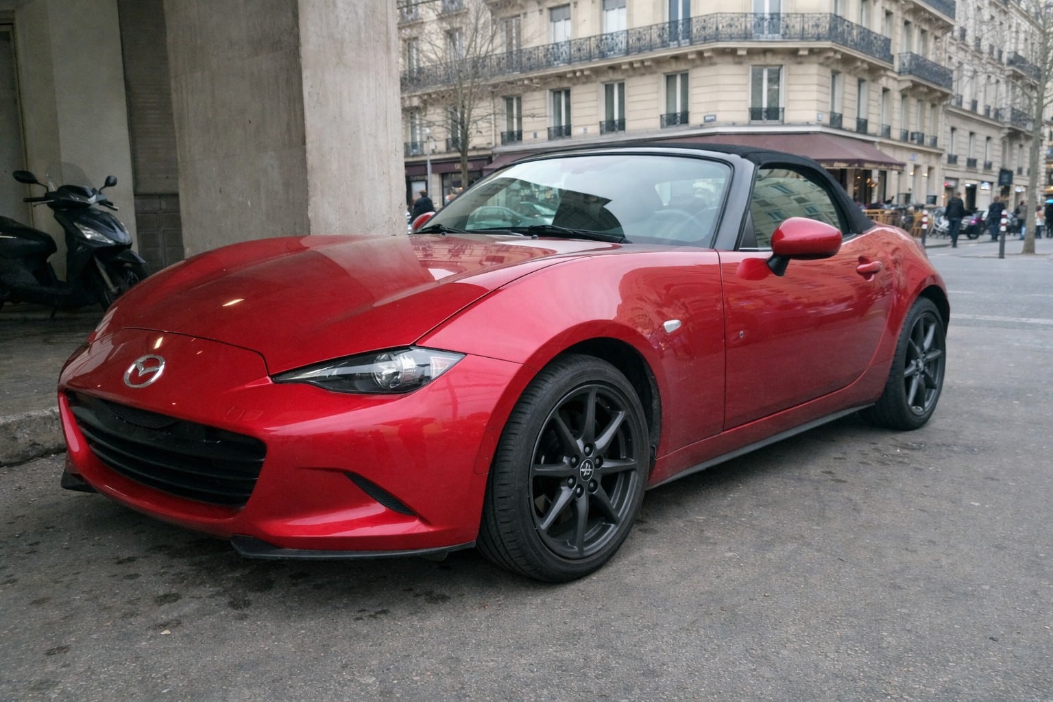 Photo d’une Mazda MX-5 ND rouge en location à Paris, stationnée en ville sous un ciel couvert, vue avant trois-quarts