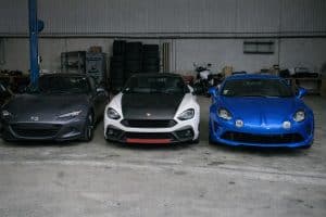 Mazda MX-5, Abarth 124 Spider et Alpine A110 garées côte à côte dans un garage pour comparer trois sportives légères emblématiques