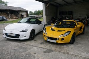 Mazda MX-5 face à Lotus Elise dans un duel de roadsters légers photographiés côte à côte dans un garage ouvert sous lumière naturelle