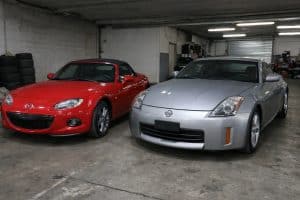 Mazda MX-5 rouge garée à côté d’une Nissan 350Z ou 370Z grise dans un garage pour un comparatif avant achat entre roadsters et coupés sportifs japonais