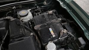 Batterie de Mazda MX-5 dans le compartiment moteur, avec cosses de batterie, support métallique, câbles électriques et éléments mécaniques visibles en gros plan