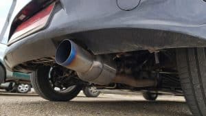 Modifications les plus populaires sur Mazda MX-5 : guide complet par génération 3 Échappement sport Invidia installé sur Mazda MX-5 ND, vue rapprochée sous le châssis arrière montrant le silencieux en inox avec sortie bleutée type titanium burn, tuyauterie et suspension visibles, photo réaliste en conditions naturelles sur parking extérieur