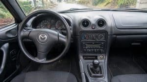 Intérieur de Mazda MX-5 NBFL avec climatisation manuelle, aérateurs ronds et tableau de bord noir, volant à gauche, vue rapprochée de la console centrale