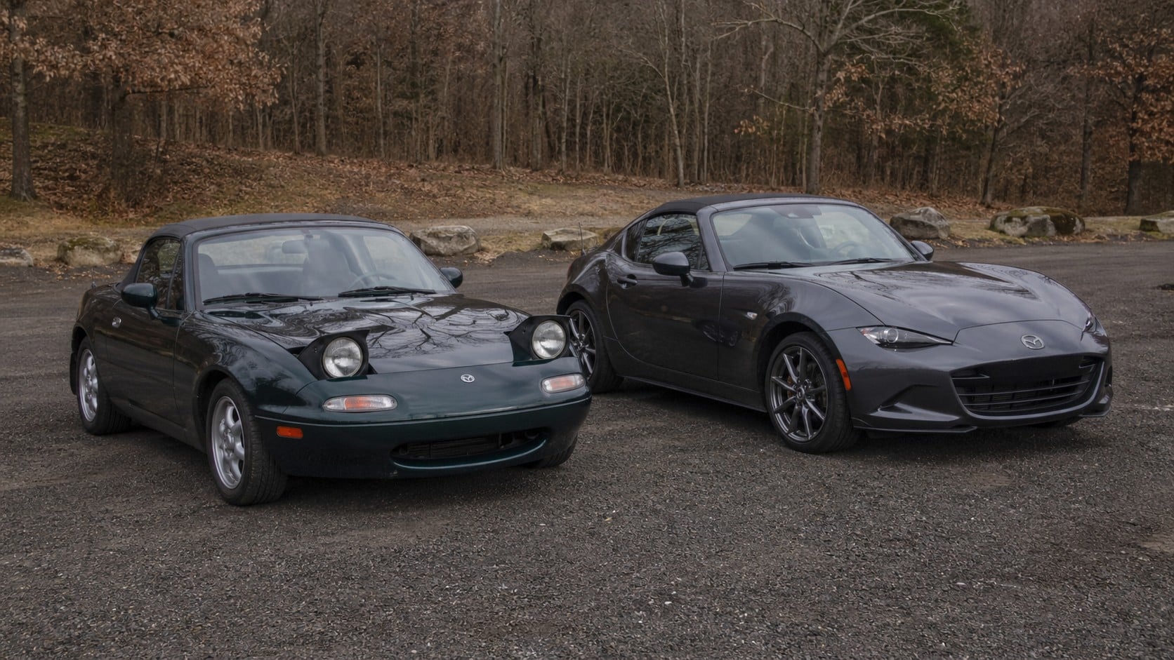Mazda MX-5 NA avec phares escamotables à côté d’une Mazda MX-5 ND grise moderne, comparatif visuel entre deux générations du roadster japonais sur parking boisé.