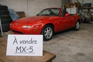 Mazda MX-5 rouge avec panneau À vendre posée dans un garage