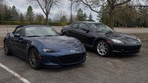 Mazda MX-5 ND bleu foncé cabriolet garé à côté d’une Mazda RX-8 noire sur un parking, comparaison visuelle entre roadster compact et coupé sportif Mazda.
