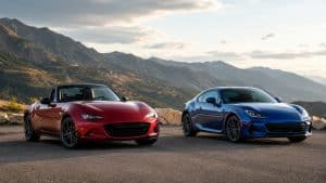 Mazda MX-5 rouge cabriolet vs Subaru BRZ bleue coupé sportif, comparatif roadster ou coupé, route de montagne au coucher du soleil, photo commerciale automobile premium, 2026, format 16:9