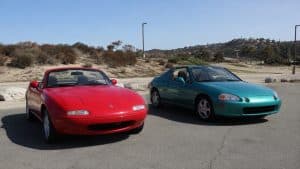 MX-5 vs Honda del Sol : quel roadster japonais choisir 3 Mazda MX-5 NA rouge décapotable face à une Honda CR-X del Sol turquoise, deux roadsters japonais des années 1990 stationnés sur une route ensoleillée, vue avant trois quarts, ciel bleu et paysage côtier, photo Canon EOS R6, 17 juillet 2026, format 16:9