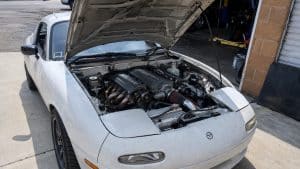 Swap V8 Mazda MX-5 : faisabilité, budget et pièges du projet 2 Mazda MX-5 NA blanche avec swap V8, capot ouvert, moteur préparé visible dans un garage automobile, photo amateur Panasonic GH4, 2026, format 16/9