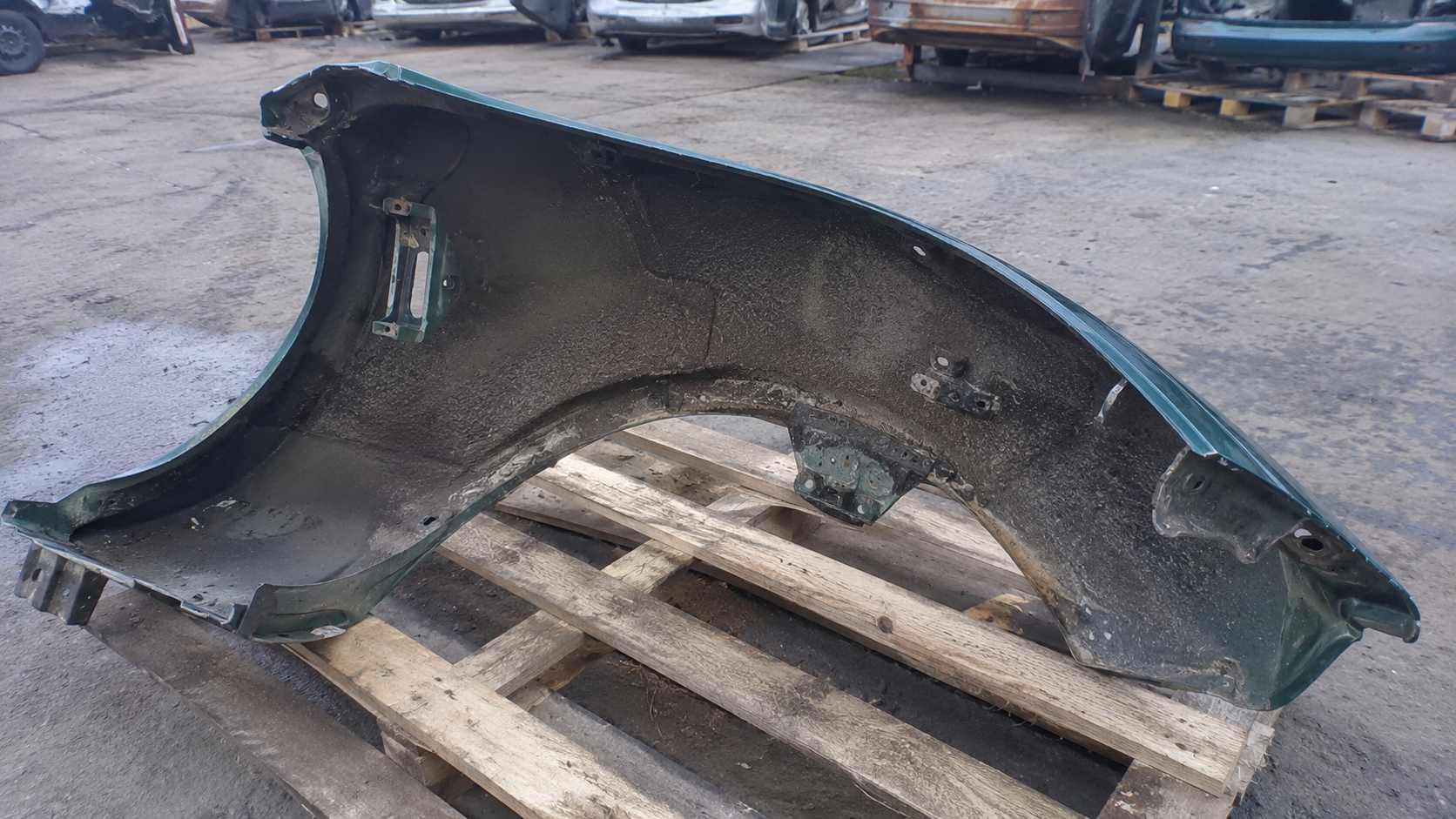 Aile avant verte de Mazda MX-5 d'occasion posée face intérieure sur une palette dans une casse auto