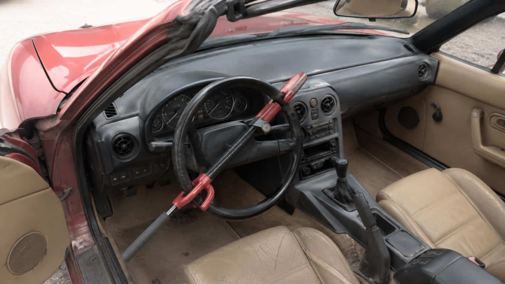 Canne antivol rouge et noire verrouillée sur le volant d'une Mazda MX-5 NA rouge à intérieur cuir beige