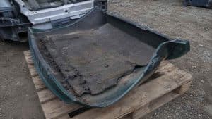 Capot vert de Mazda MX-5 retourné sur une palette en casse auto, insonorisant usé apparent