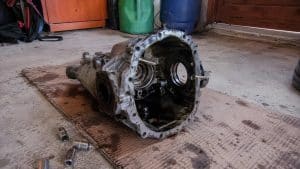Carter de différentiel de Mazda MX-5 ouvert et vidé posé sur un carton au sol d'un garage, douilles autour