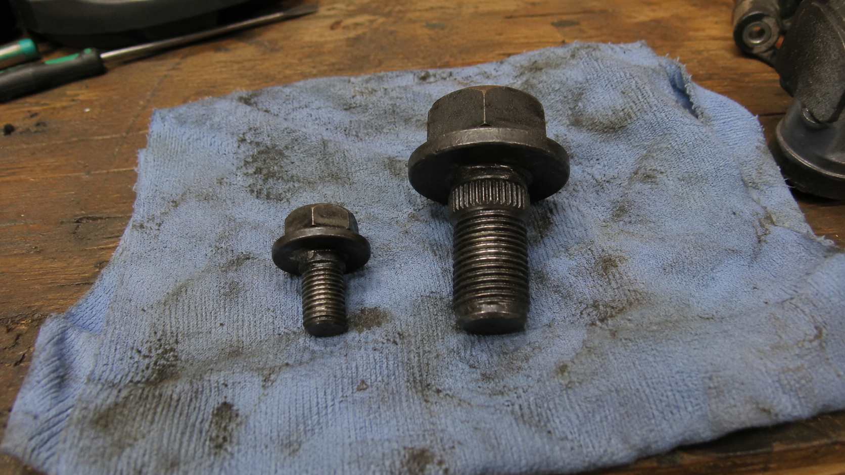 Comparaison de deux boulons de poulie de vilebrequin de Mazda MX-5 posés sur un chiffon d'atelier bleu