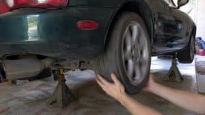 Contrôle du jeu de la roue arrière d'une Mazda MX-5 NB verte sur chandelles, mains sur le pneu