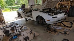 Mazda MX-5 NA blanche en démontage complet, pièces mécaniques étalées au sol du garage