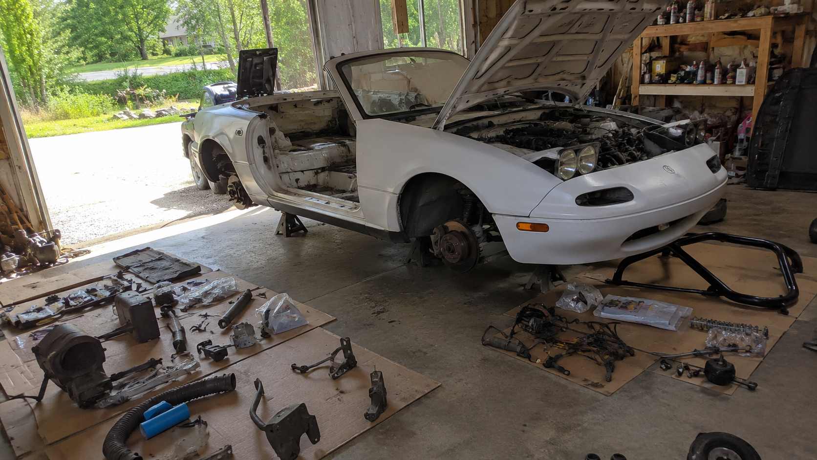 Mazda MX-5 NA blanche en demontage complet, pieces mecaniques etalees au sol du garage