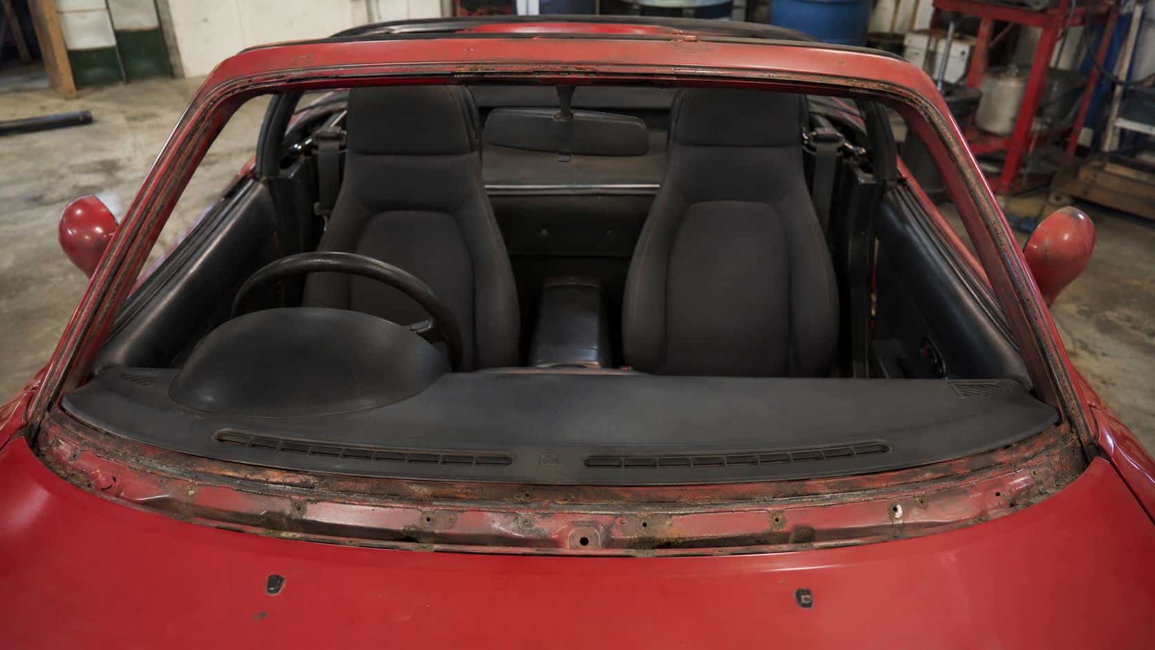 Mazda MX-5 NA rouge en atelier avec pare-brise déposé laissant apparaître un cadre de baie corrodé