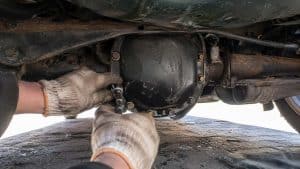 Desserrage au cliquet des boulons du carter de différentiel arrière sous une Mazda MX-5 verte, mains gantées