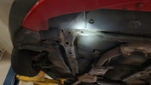 Dessous de caisse d'une Mazda MX-5 rouge sur pont élévateur, longerons et ligne d'échappement inspectés à la lampe
