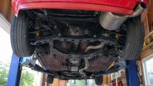 Dessous d'une Mazda MX-5 NA rouge sur pont élévateur montrant la poutre PPF et la ligne d'échappement inox